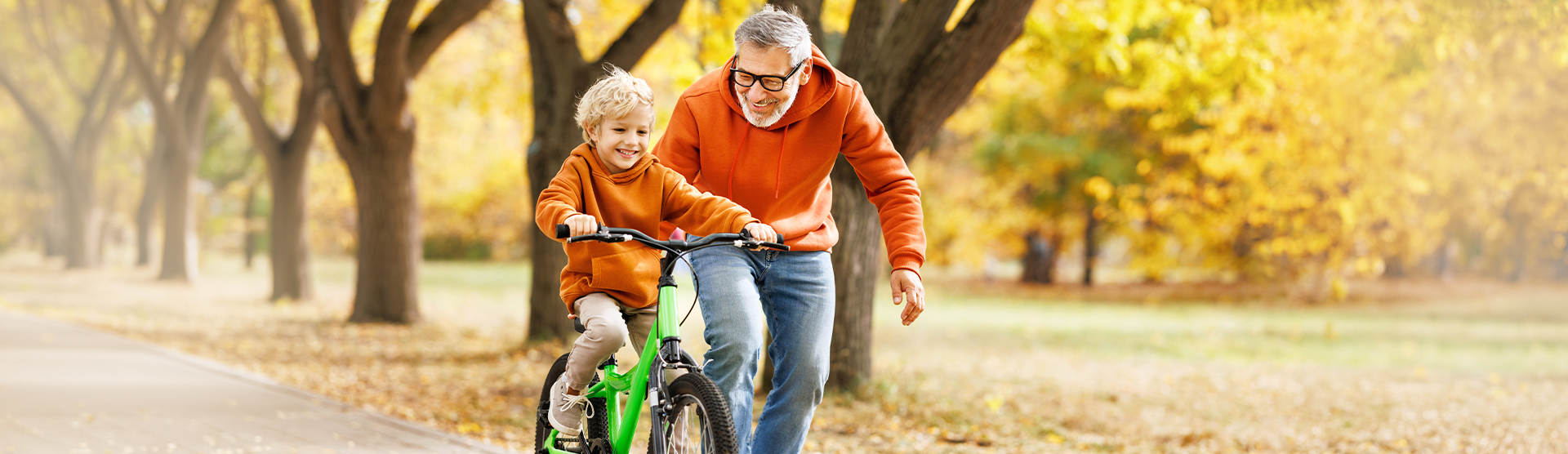 Blonder Junge wird von seinem Großvater in einem herbstlichen Park auf dem Fahrrad angeschoben